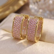 Gold-tone square hoop earrings with pink stones on pale fabric