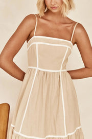 Close view of square neckline and white trim on tan dress
