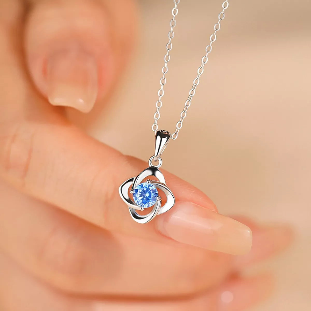 Close view of blue zircon clover pendant held between fingers