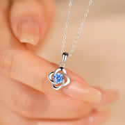 Close view of blue zircon clover pendant held between fingers