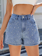 Blue high-waisted denim shorts with scattered silver-coloured studs on the front, worn with a white crop top