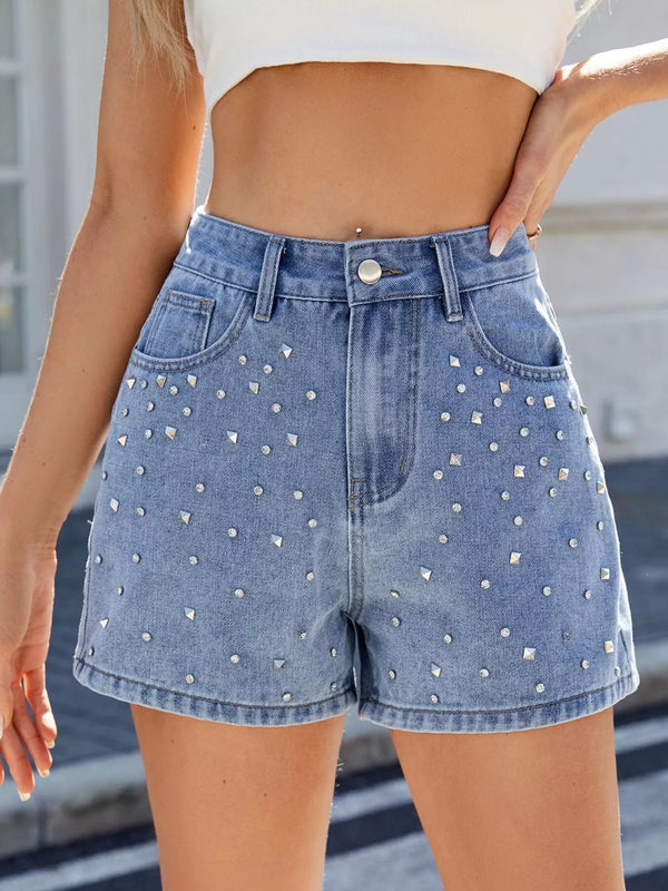 Blue high-waisted denim shorts with scattered silver-coloured studs on the front, worn with a white crop top