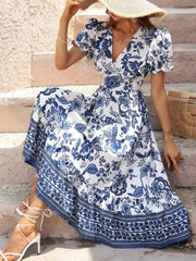 Blue and white floral midi dress with puff sleeves and a patterned border hem, shown seated.