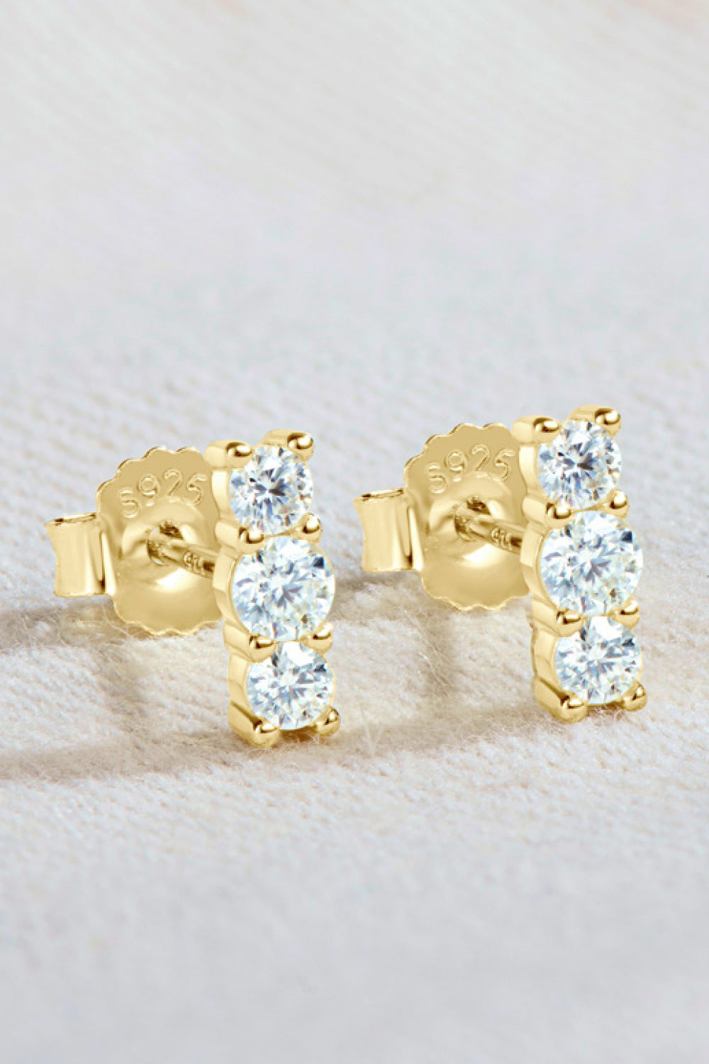 Pair of three-stone vertical moissanite studs on textured surface