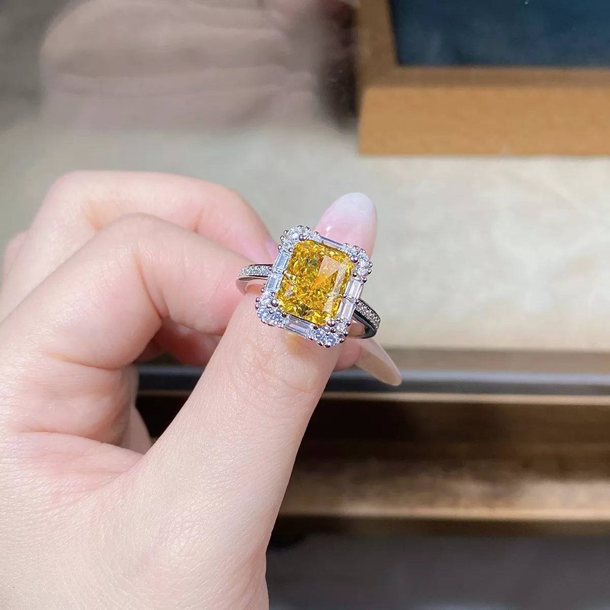 Close view of a rectangular yellow gemstone ring with clear-stone halo