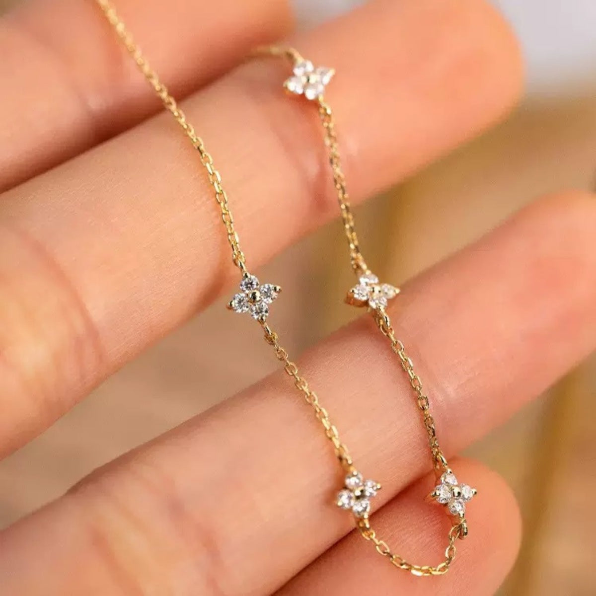 Gold-tone clover charm bracelet draped over fingertips