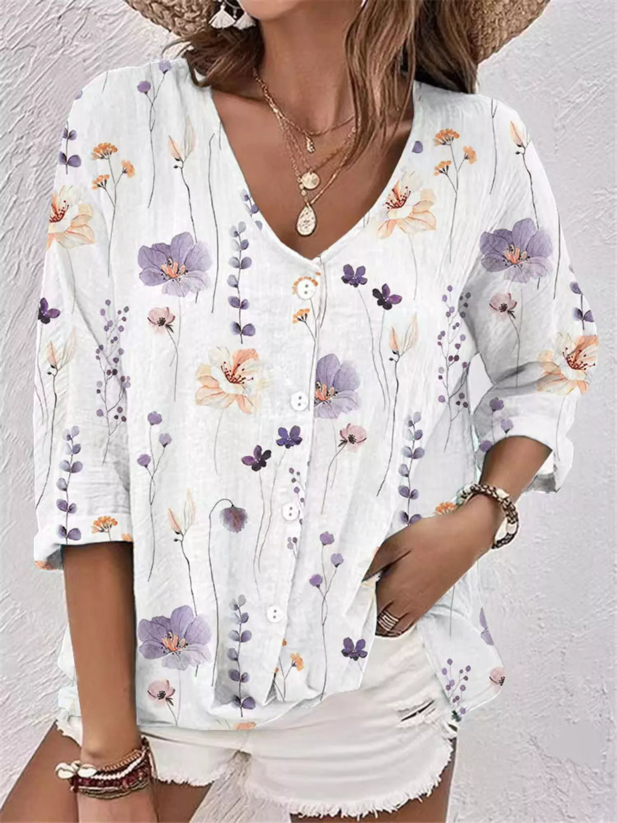 Model wearing white floral blouse with colorful flowers and white shorts.