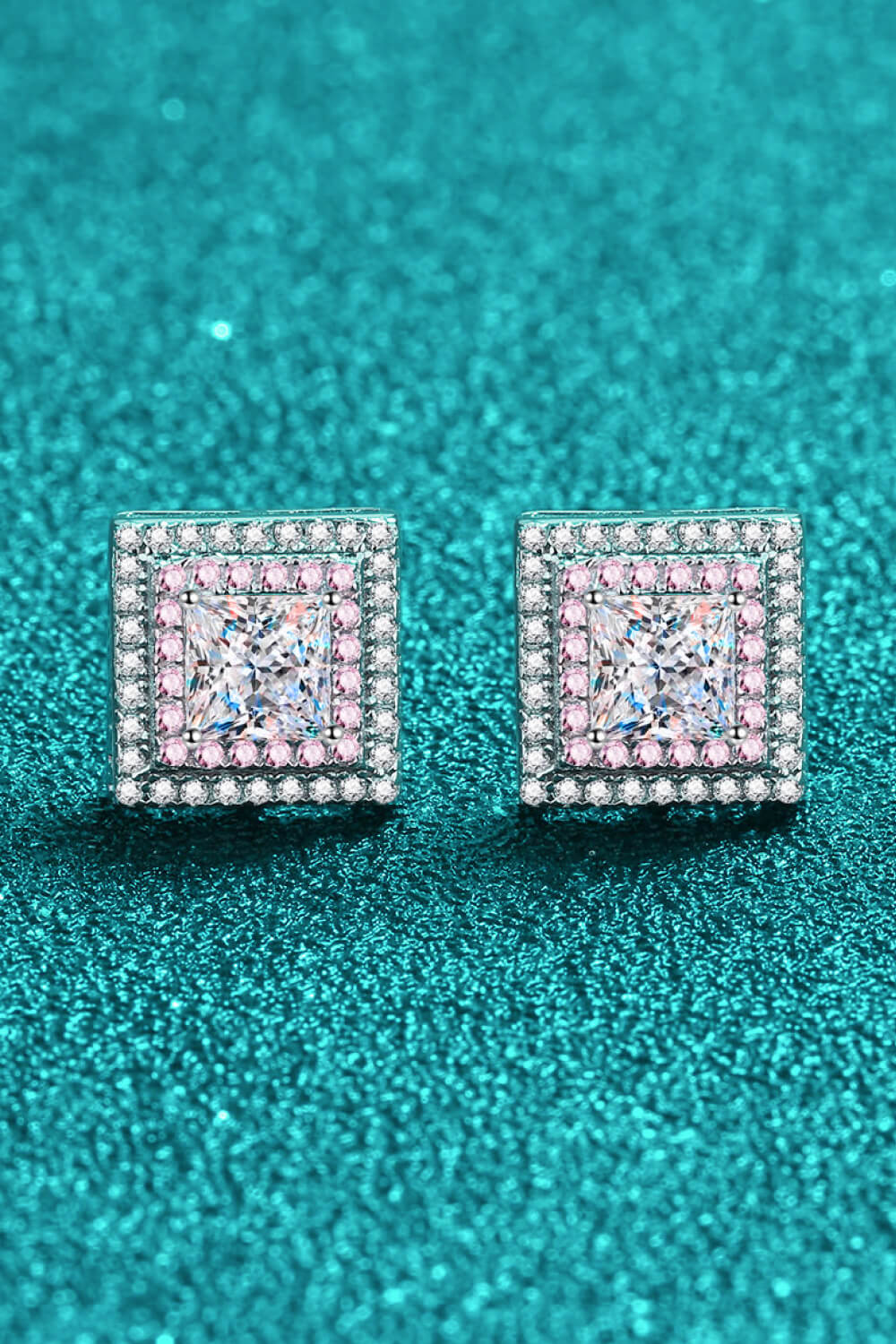 Pair of square pink-and-clear stone studs on a teal textured surface