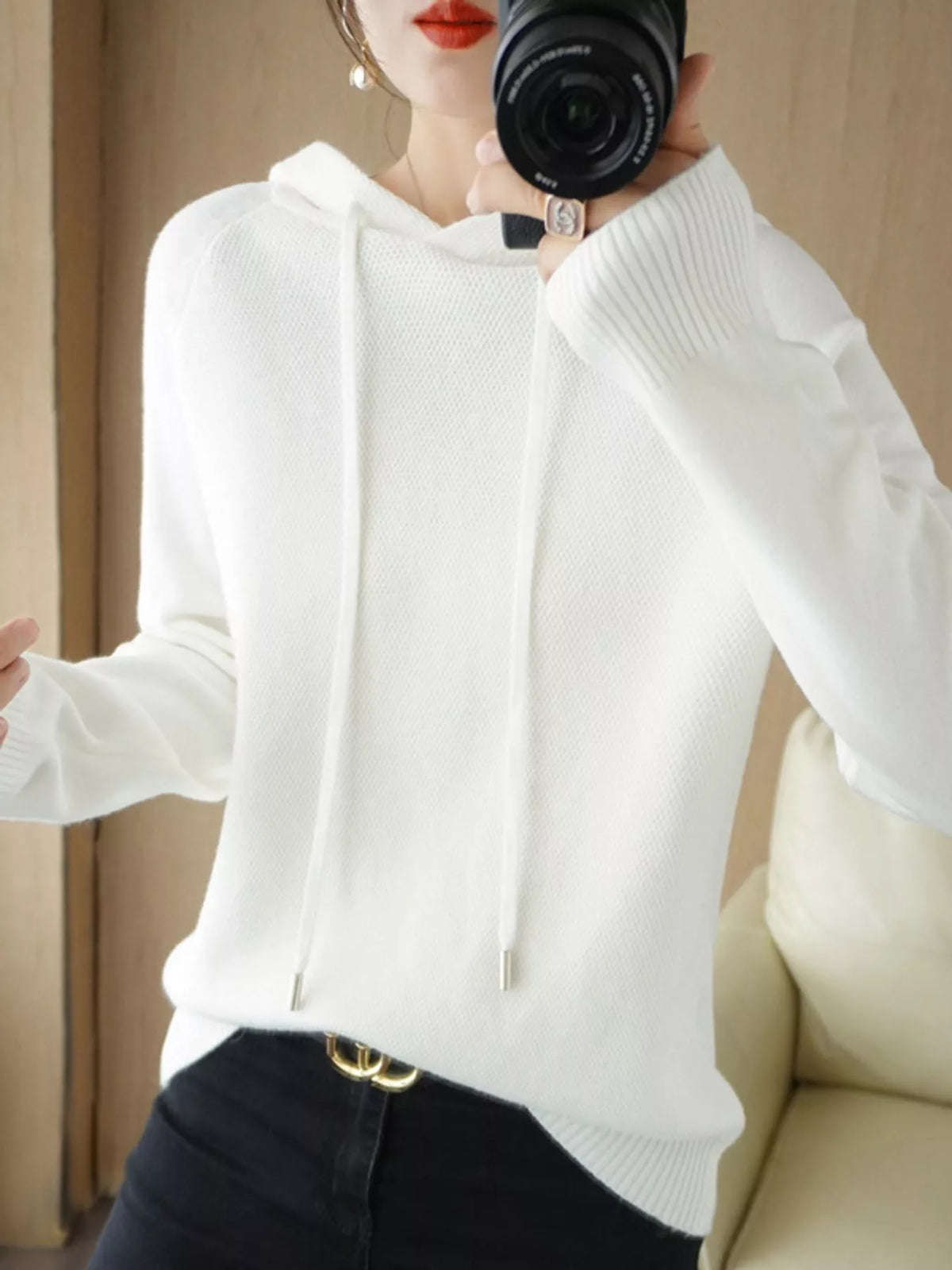 White hooded sweater shown in a front mirror photo with black trousers.