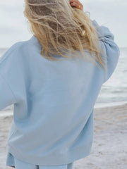 Back view of a light blue crewneck sweatshirt on a model at the beach.