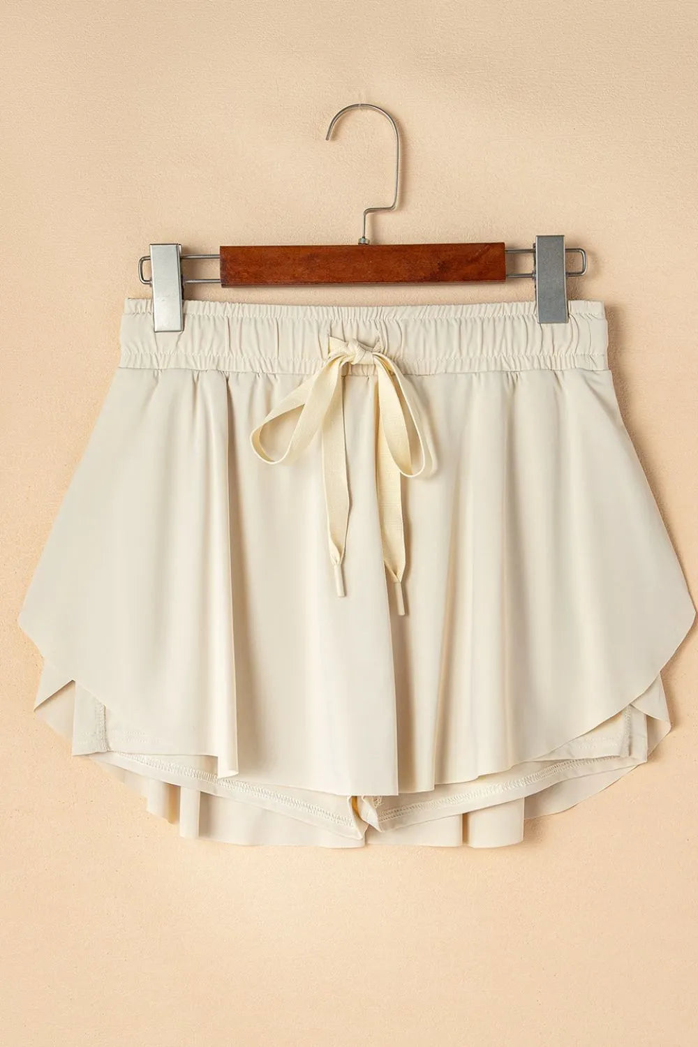 Ivory skort displayed on a wooden hanger, showing front tie and layered hem.