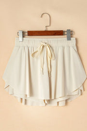 Ivory skort displayed on a wooden hanger, showing front tie and layered hem.