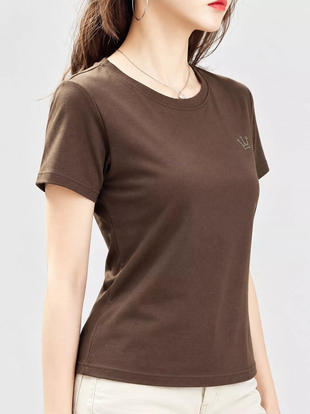 Brown short-sleeve T-shirt with small crown emblem, shown on a model from the front at an angle.