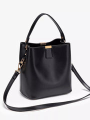 Angled front view of a black bucket bag showing the open top, short handle, and long shoulder strap.