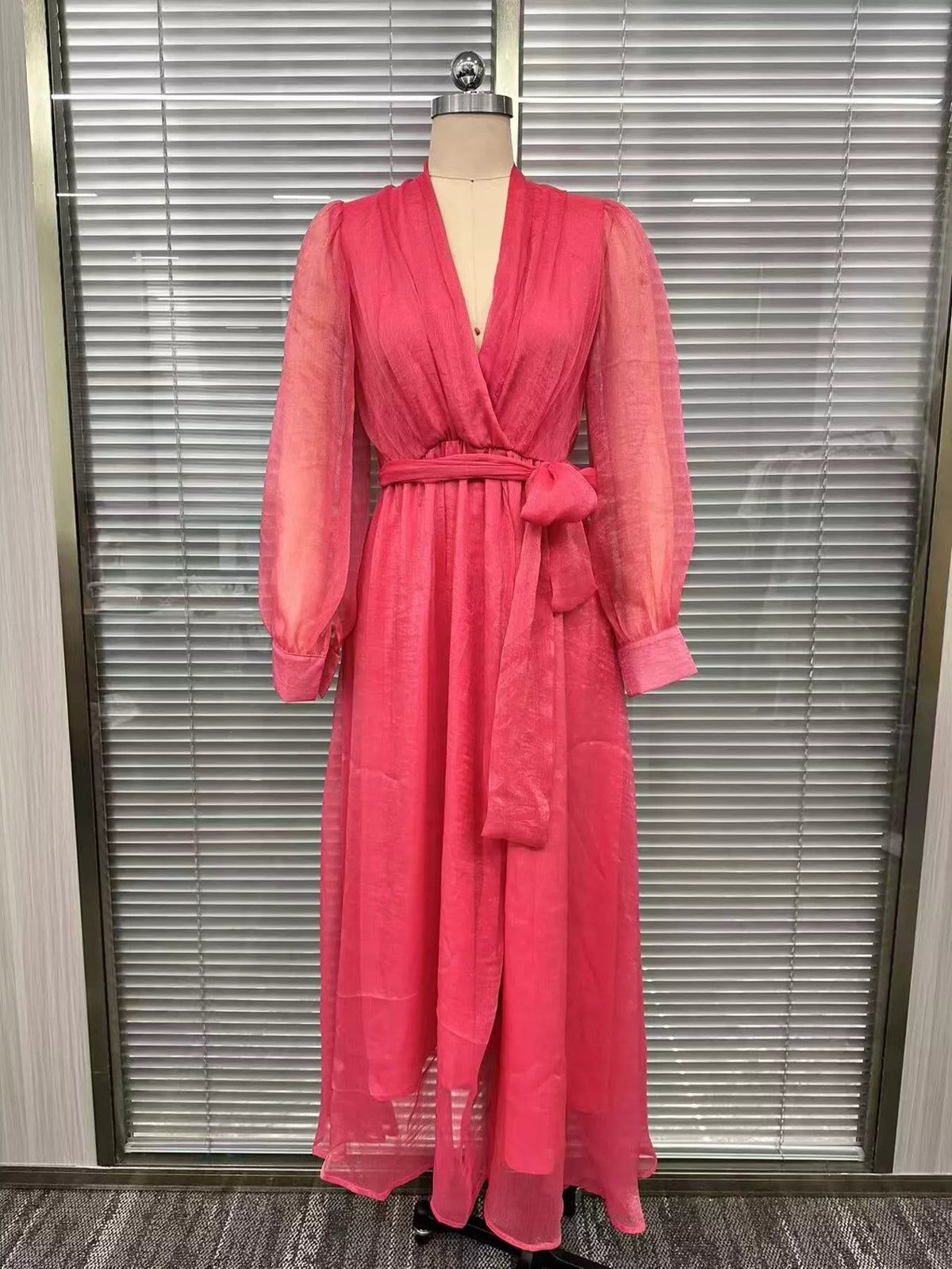 Front view of the pink long-sleeve wrap maxi dress with a waist tie on a dress form.