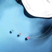 Three silver-tone zircon pendant necklaces in pastel blue, pink and lavender on a blue display