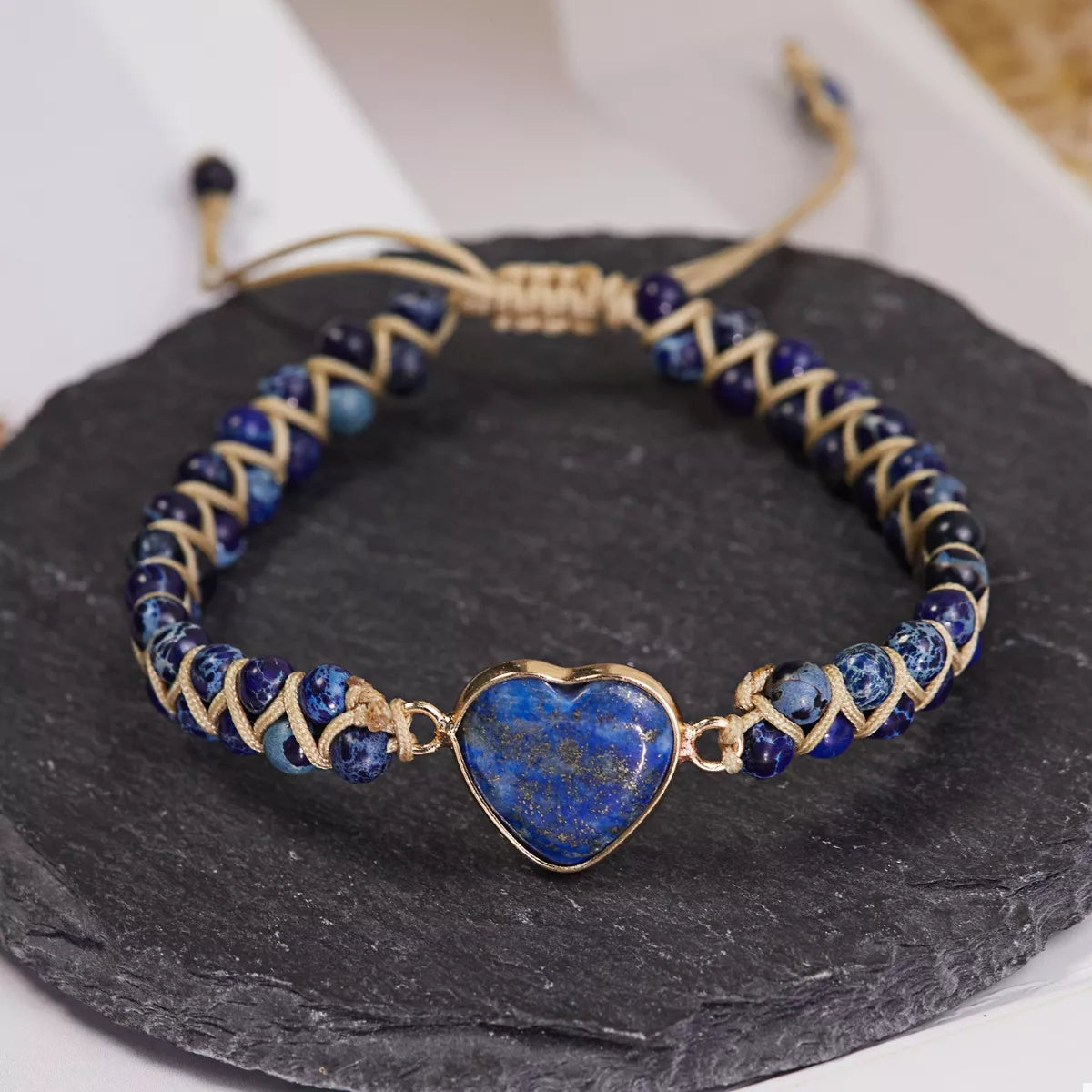 Front view of a blue heart bracelet with navy beads and gold-tone woven details on slate.