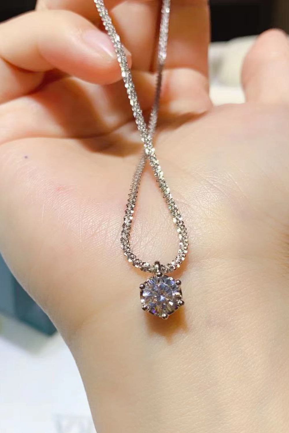 Round clear-stone pendant necklace held over an open hand