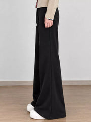 Black wide-leg trousers shown from the side with white shoes and a beige top