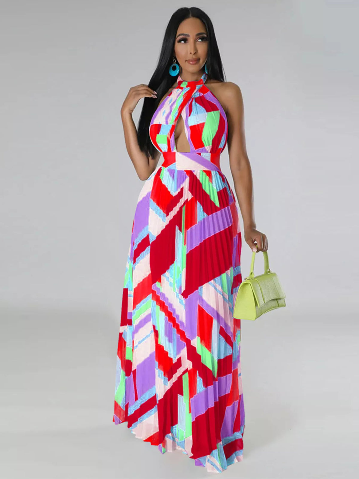 Model in a red and pink geometric halter dress holding a light green handbag at her side.