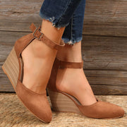 Tan pointed-toe sandals worn from a rear side angle showing wedge heels