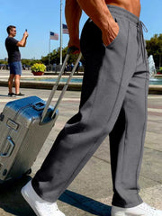 Side view of charcoal gray pants with a hand in the pocket beside a rolling suitcase.