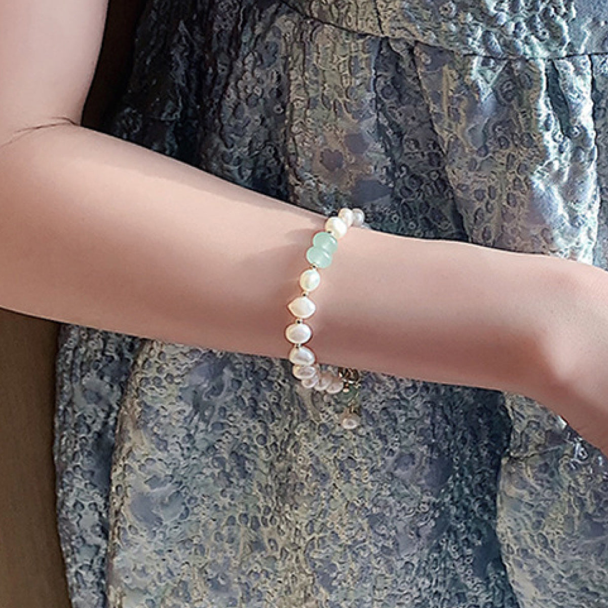 Bracelet with alternating white pearls and pale green stones on a wrist