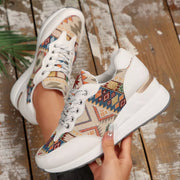 Close view of cream lace-up wedge sneakers with colorful woven-look panels, held in hand