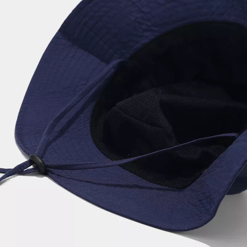 View beneath the navy bucket hat shows its interior and chin cord attachment.