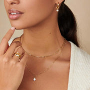 Model wearing a delicate gold-tone pendant necklace with a white cardigan