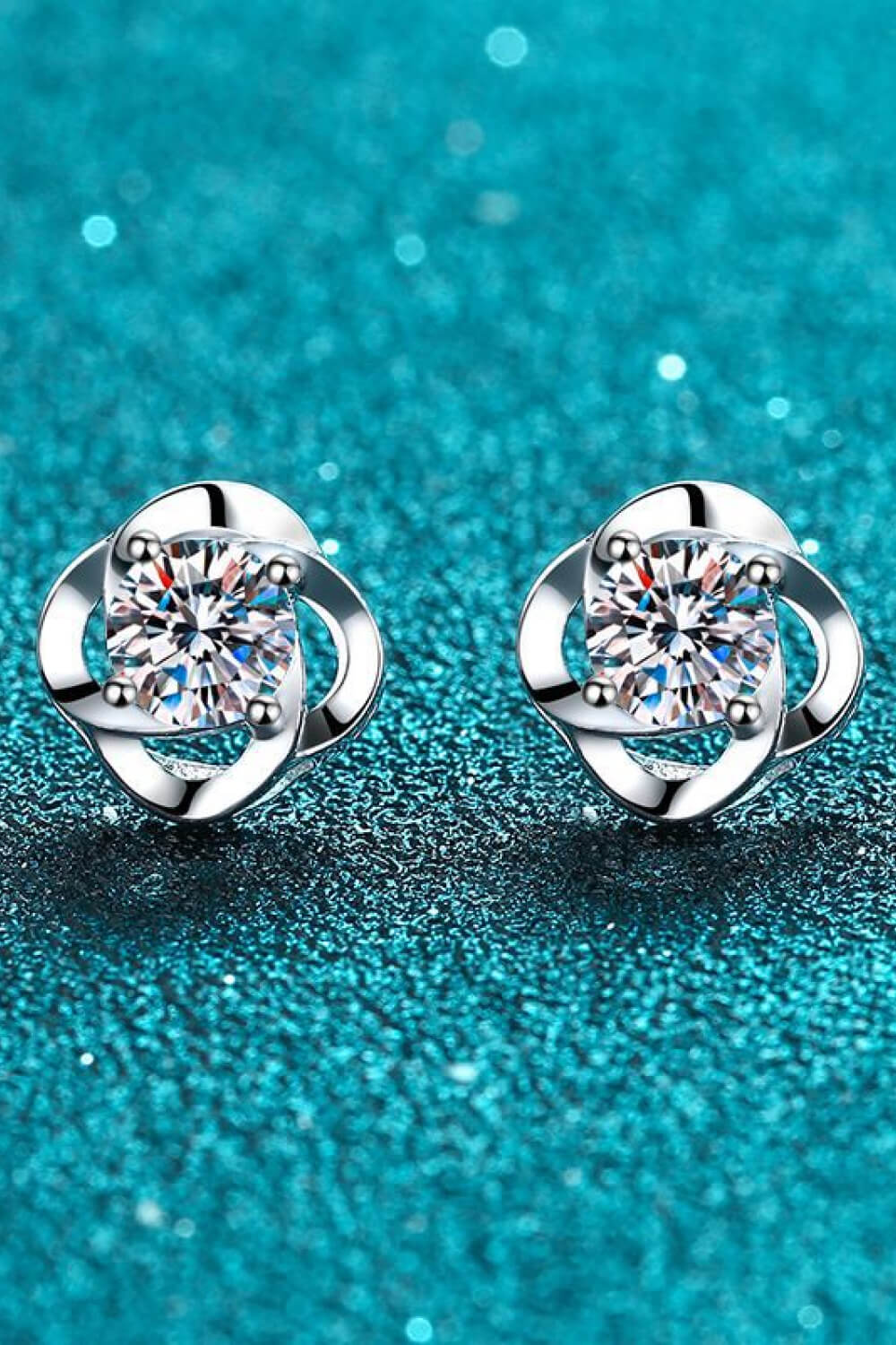 Clear-stone stud earrings with silver-tone curled surrounds on a teal surface