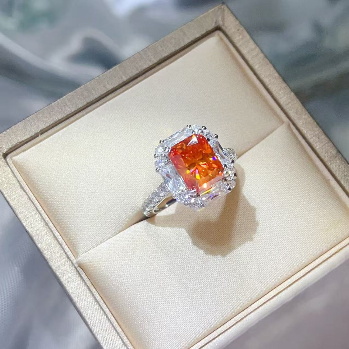 Orange rectangular center stone ring with clear halo in box