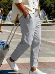 White pants styled with an overshirt beside a suitcase in a plaza.