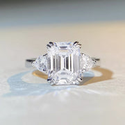 White-metal ring with a large clear emerald-cut center stone and two side stones, front view
