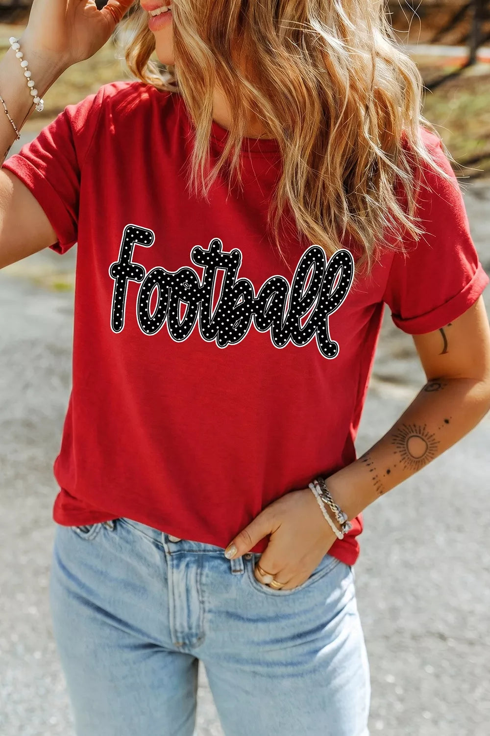 Front view of red Football lettering T-shirt with one hand in jeans pocket