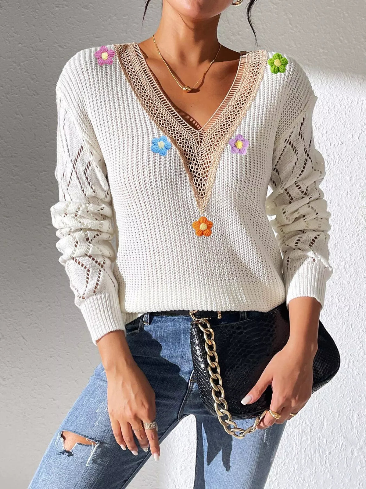 White V-neck floral sweater worn with jeans and a black chain-strap bag.