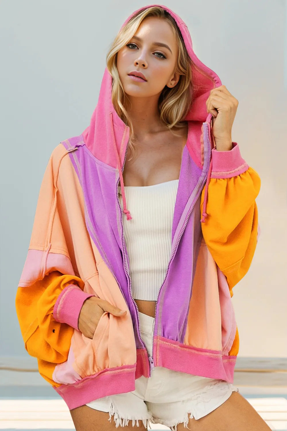 Back view of pink, peach, and orange color-block hoodie with hood and zip closure.