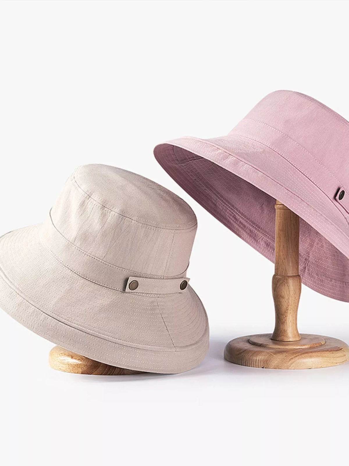 Pink and khaki wide-brim sun hats displayed on wooden stands
