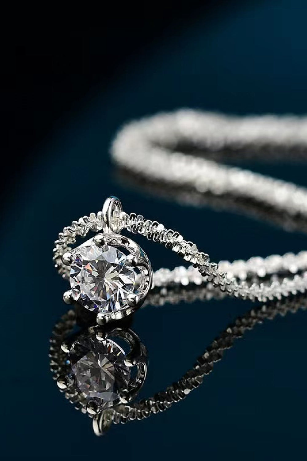 Close-up of a round clear-stone pendant and chain on a dark reflective surface