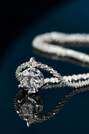 Close-up of a round clear-stone pendant and chain on a dark reflective surface