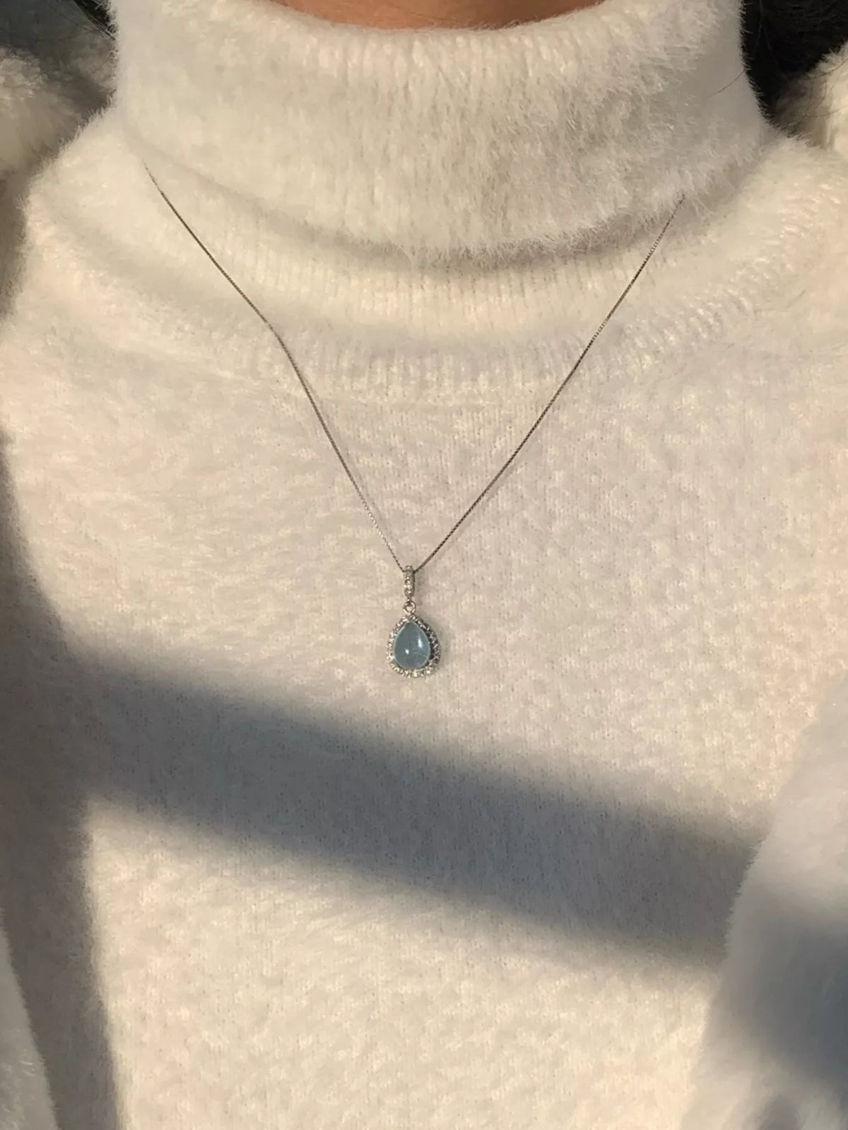 Small crystal teardrop pendant on fine chain, worn over a light turtleneck