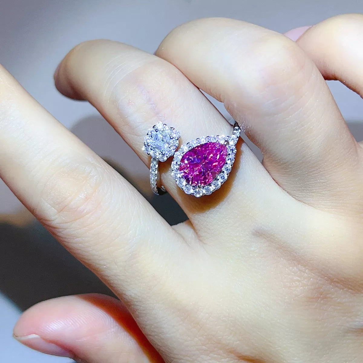 Pink pear-shaped bypass ring with clear-stone cluster worn on hand