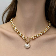 Close view of chunky pearl chain necklace and heart pendant worn at the neck