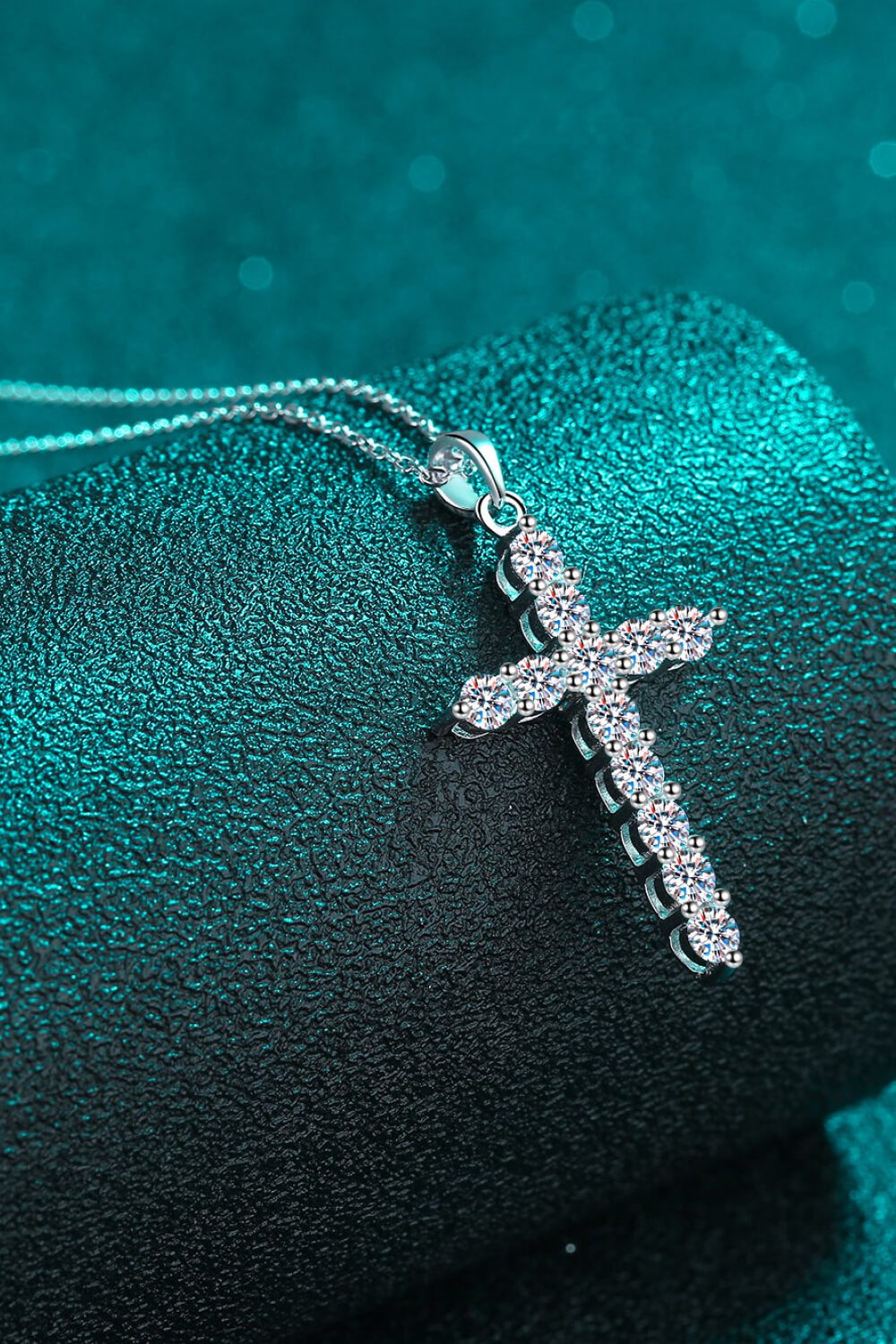 Silver-tone moissanite cross pendant resting on teal fabric