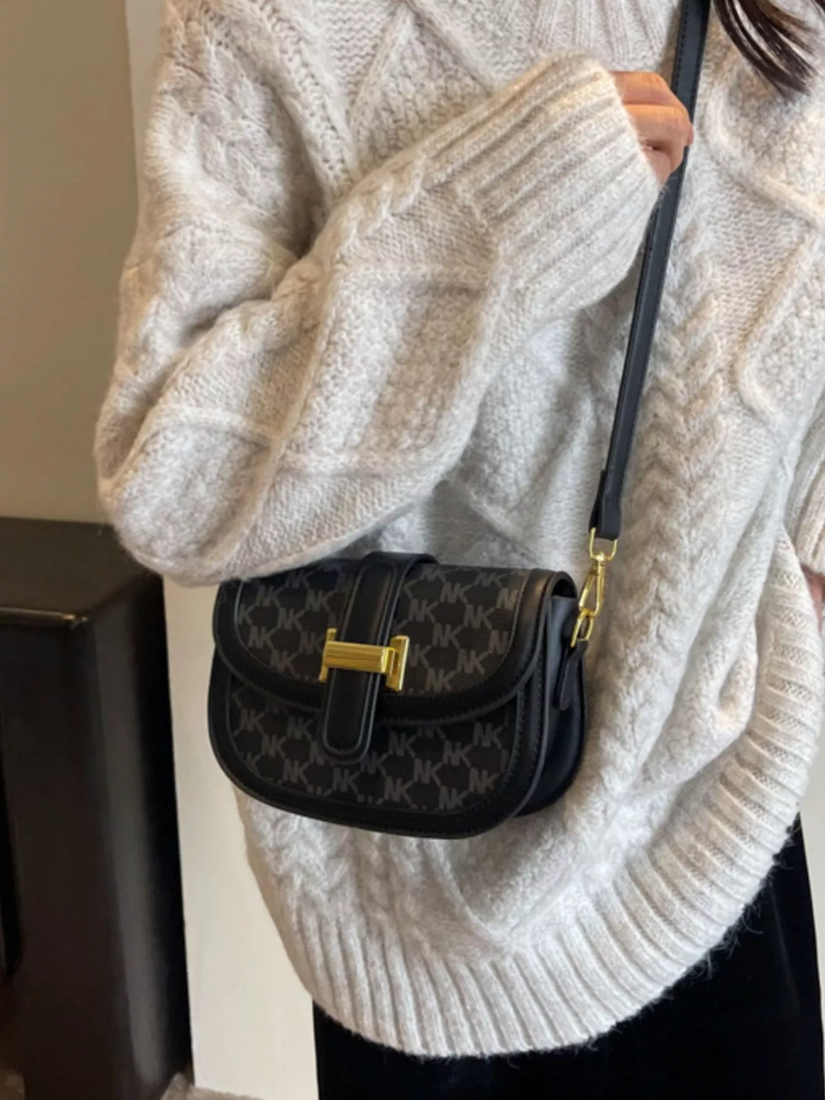 Black patterned flap bag worn on a long black strap with gold-coloured attachments