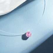 Pink round zircon pendant necklace with a fine silver-tone chain on blue fabric