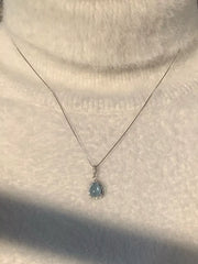 Silver-tone teardrop necklace worn close-up against a cream sweater
