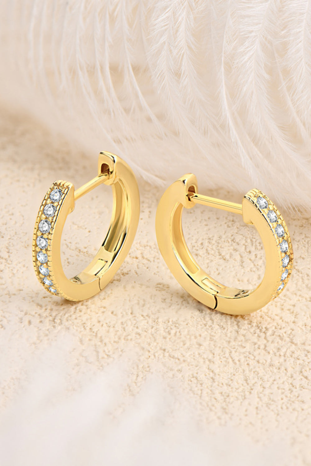 Pair of gold-tone stone-set hoops displayed open against a soft textured background