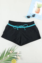 Black swim shorts with turquoise stripe and tied drawstring, displayed flat with beach accessories.
