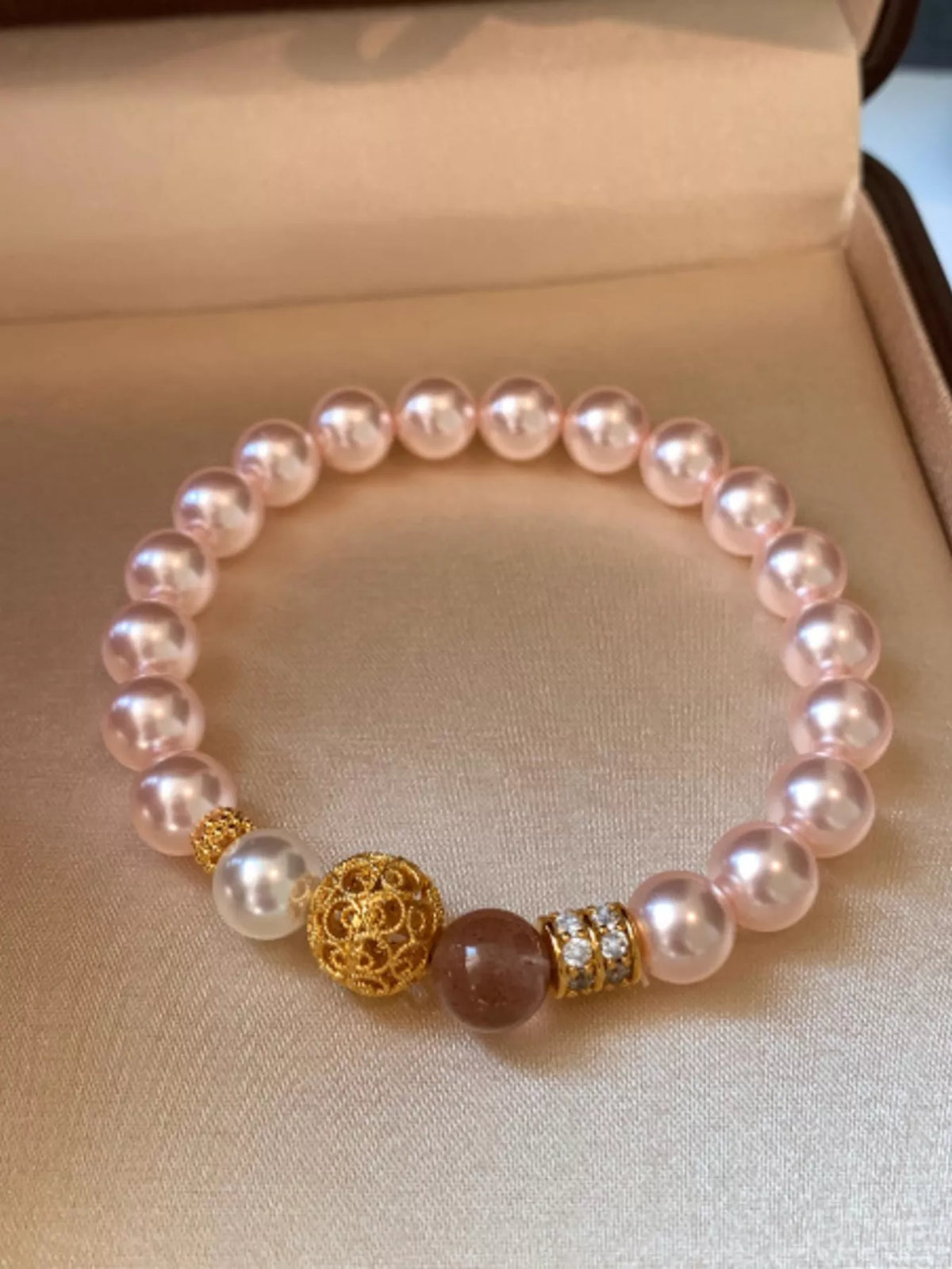 Blush pearl bracelet with a gold filigree centerpiece and mauve accent bead in a jewelry box